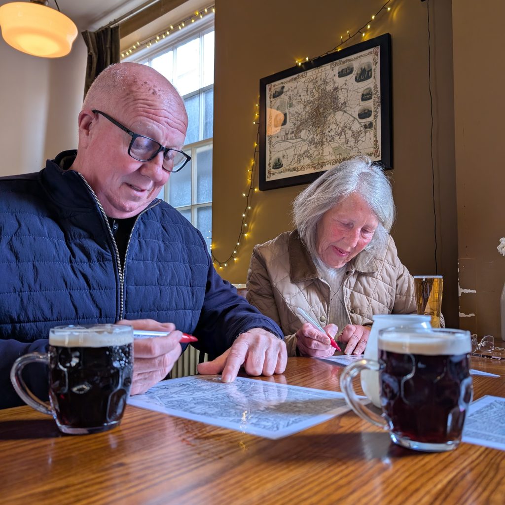 Tour guests with drinks looking at old maps whilst in the Lamb and Flag