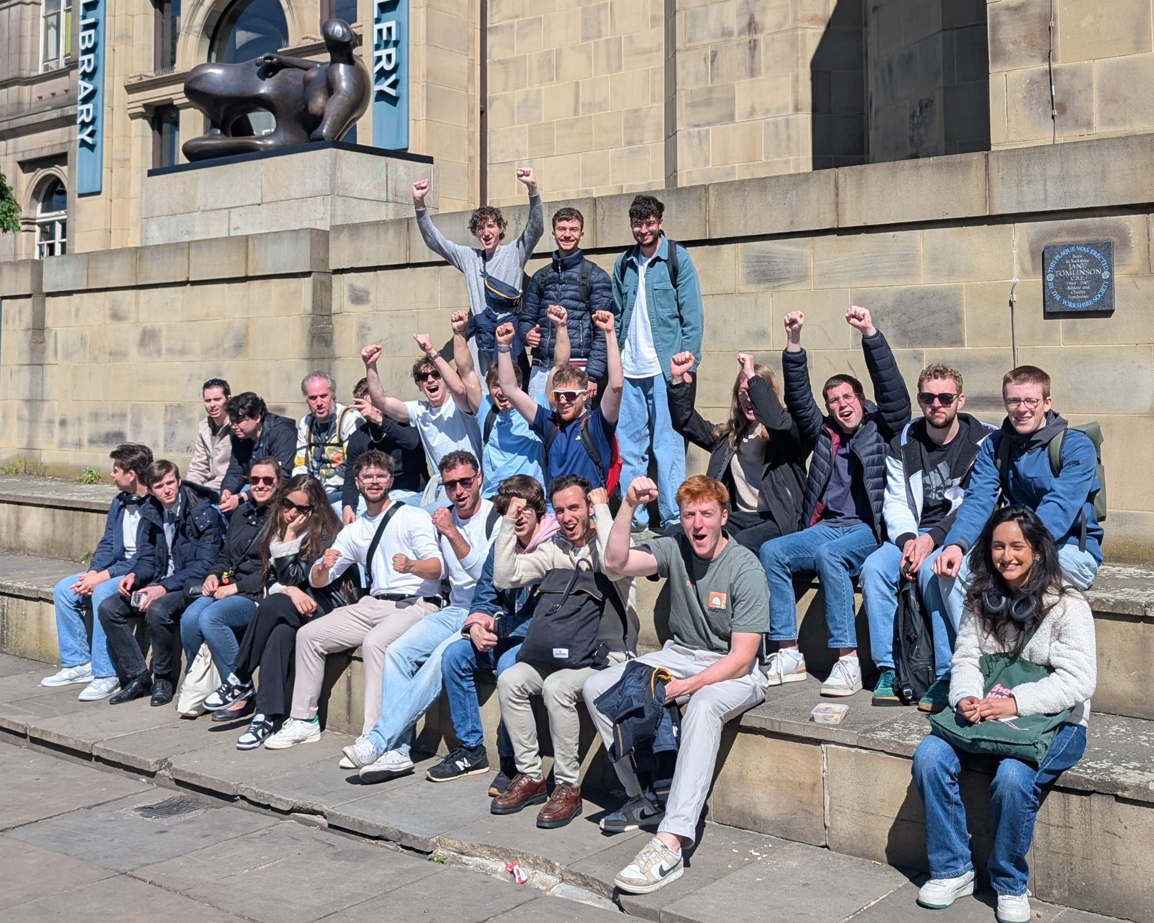 Tour guests raising their arms in celebration whilst seated outside Leeds Art Gallery